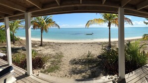 A beach view from a covered area with palm trees and a boat on the water.