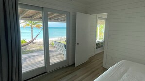 A bedroom with a large bed, a sliding glass door leading to a balcony with a hammock and a view of the beach.