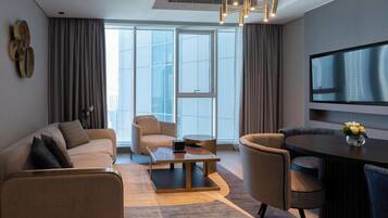 Una habitación de hotel moderna con sofá, sillón, mesa de comedor y televisor en la pared.