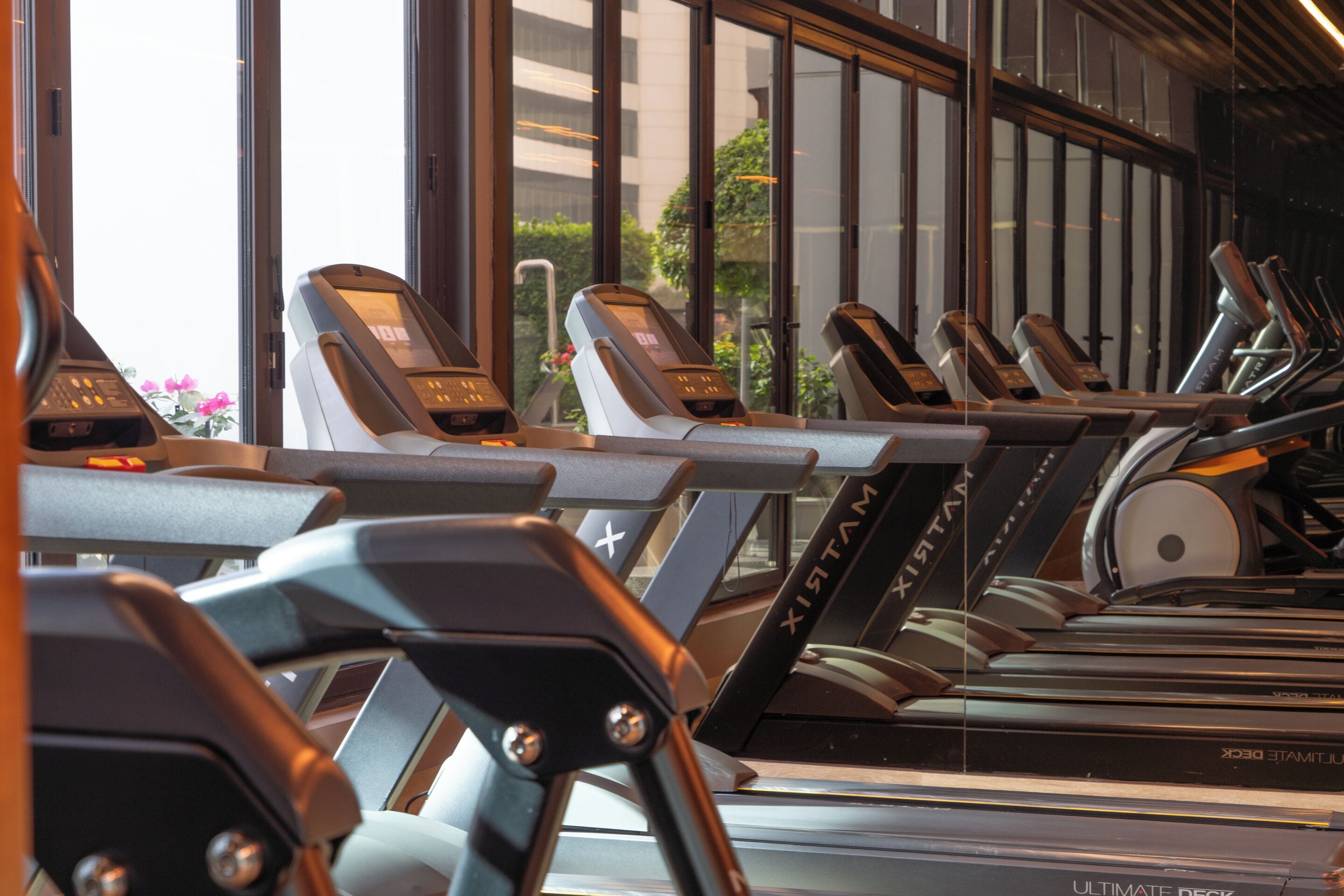 En rad löpband med digitala displayer, placerade i ett gym med stora fönster och utsikt över byggnaderna utanför.