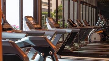 En rad löpband med digitala displayer, placerade i ett gym med stora fönster och utsikt över byggnaderna utanför.