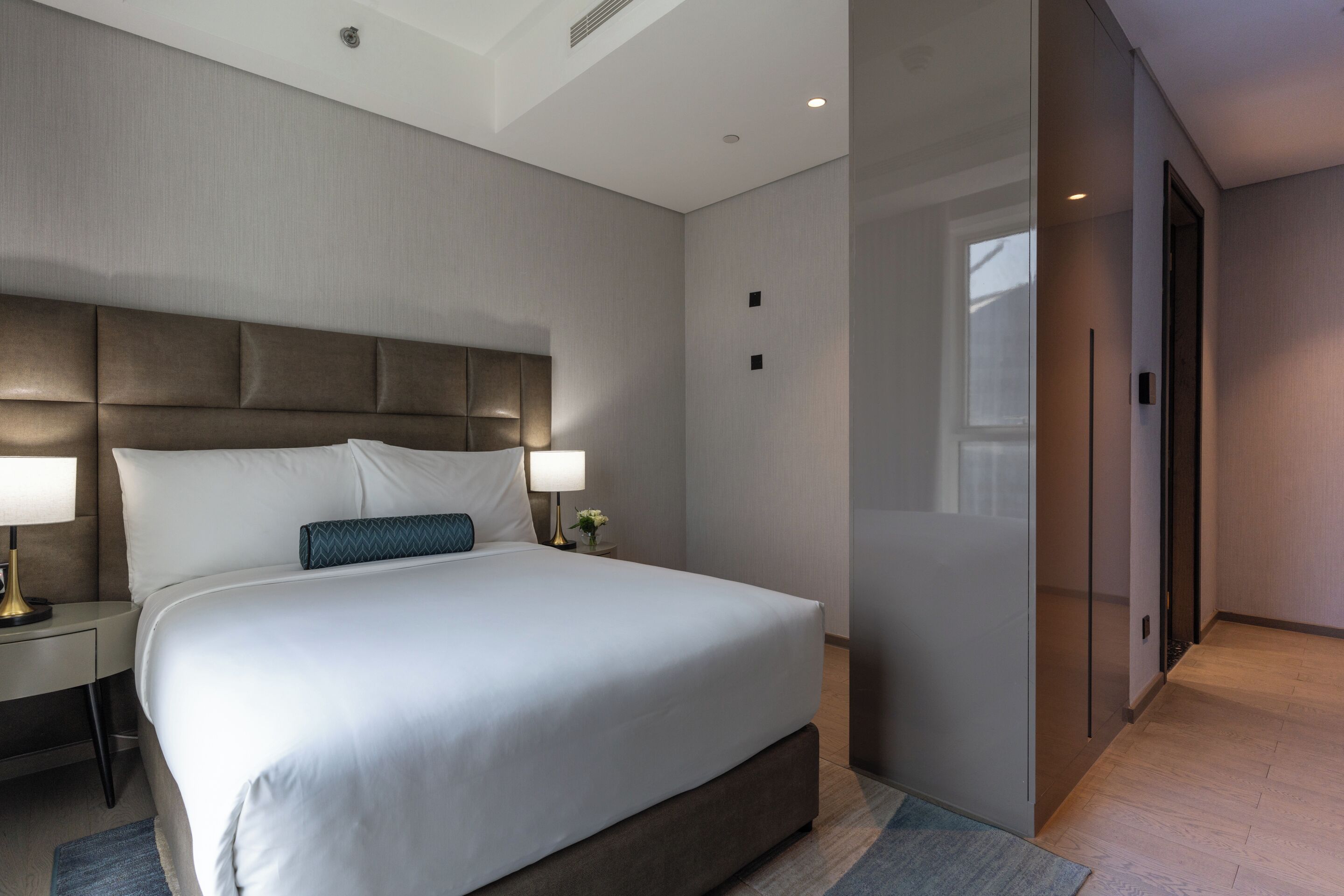 Una habitación de hotel moderna con una cama grande, lámparas de noche, una mesita de noche y un separador de vidrio.