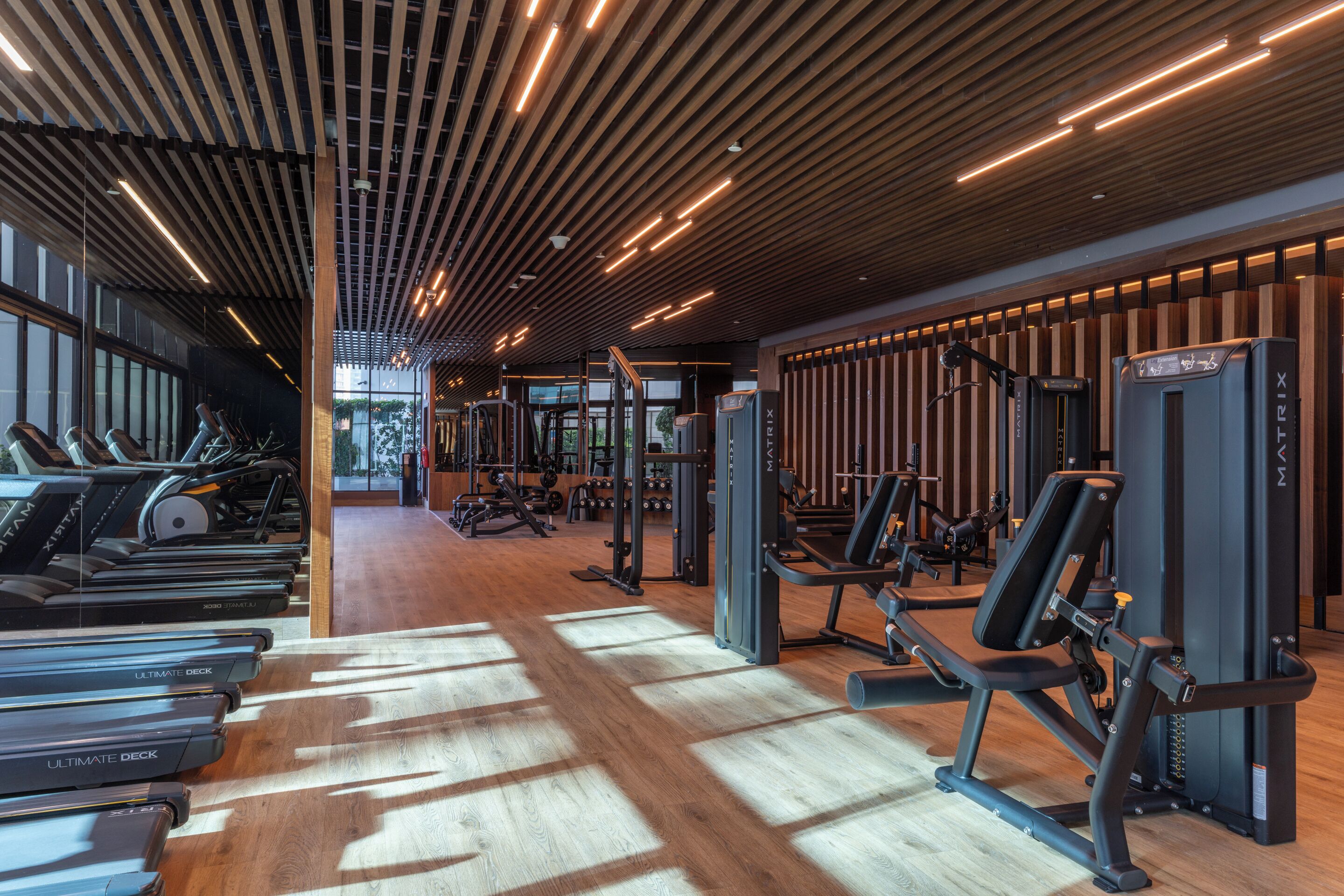 Et fitnesscenter med løbebånd, styrkemaskiner og et træloft.