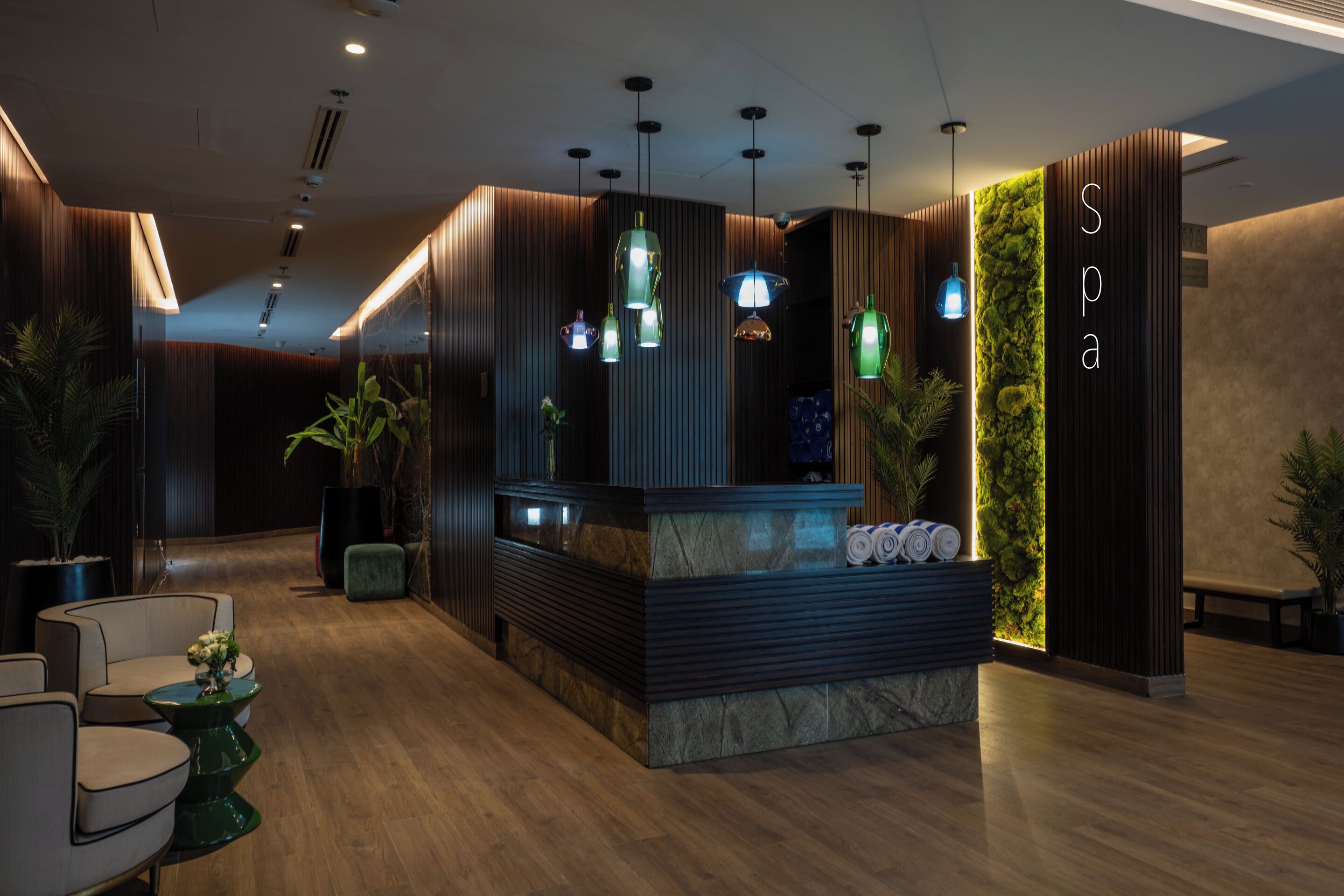 A reception area with a reception desk, multiple hanging pendant lights, and a wall with a vertical garden.