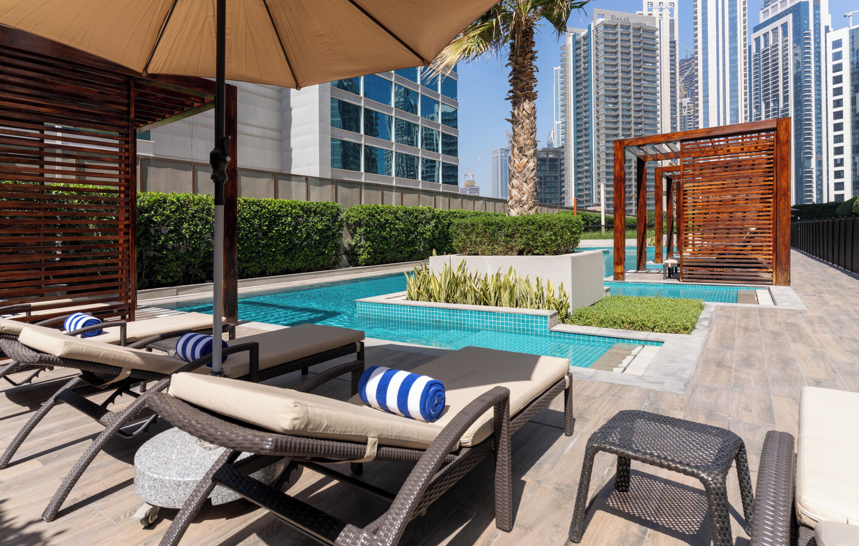 A rooftop pool area with lounge chairs, a small table, and a pergola.