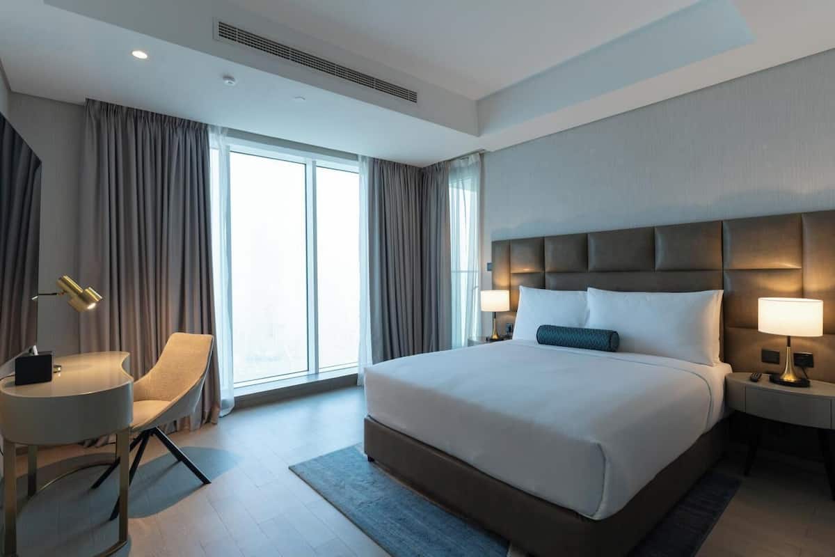 A modern hotel room with a large bed, a desk, and a chair.