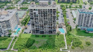 A high-rise hotel with multiple balconies, a swimming pool, and a beach area.