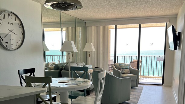 A modern living room with a dining area, large windows, and a view of the sea.