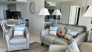 A modern living room with a grey sofa, striped rug, and beach-themed cushions.