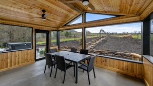 Un intérieur en bois avec une table et des chaises, de grandes fenêtres et une vue sur un espace extérieur agrémenté d’un mur en pierre.