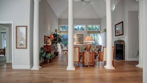 A spacious living room with wooden flooring, white columns, a fireplace, and a large window with a view of greenery. - 3 Sprunt Pond at The Sea Pines Resort (Hilton Head Island)