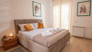 Una cama bien hecha con cabecera, una mesita de noche con lámpara y un radiador.