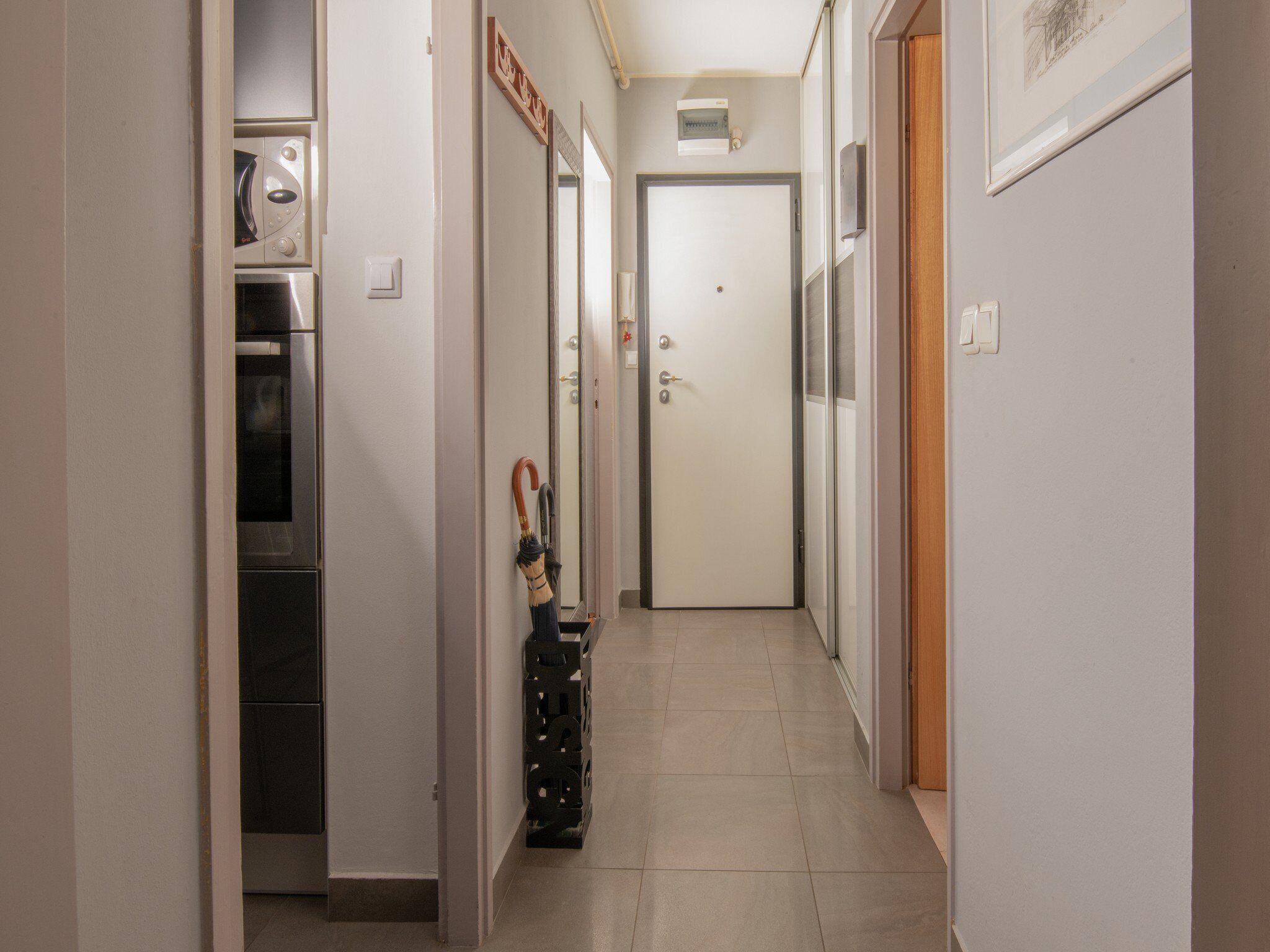 A narrow hallway with a microwave, a door with a handle, and a wall-mounted light fixture.