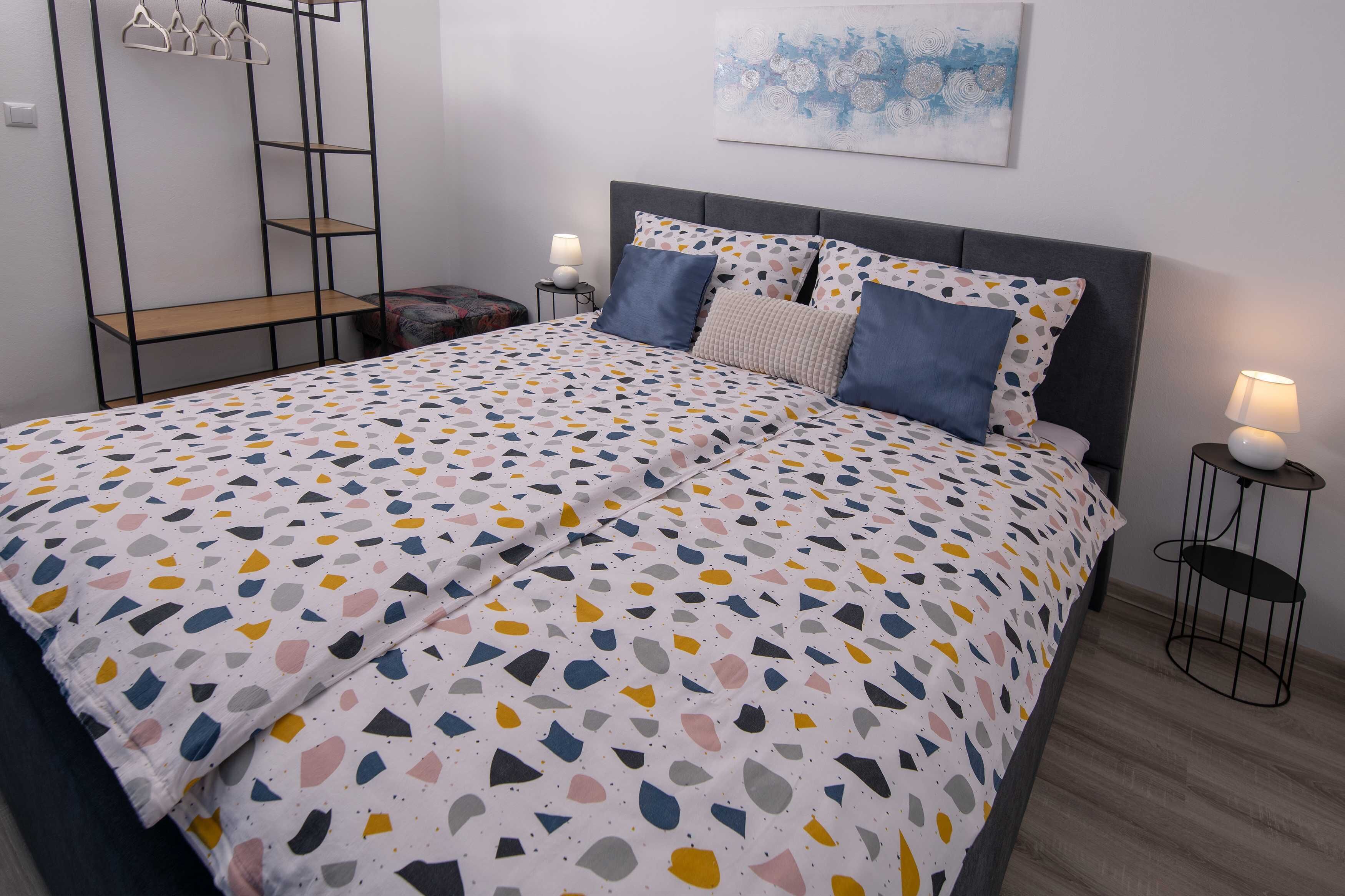 A bedroom with a bed, a bedside table with a lamp, a wall-mounted shelf, and a painting.