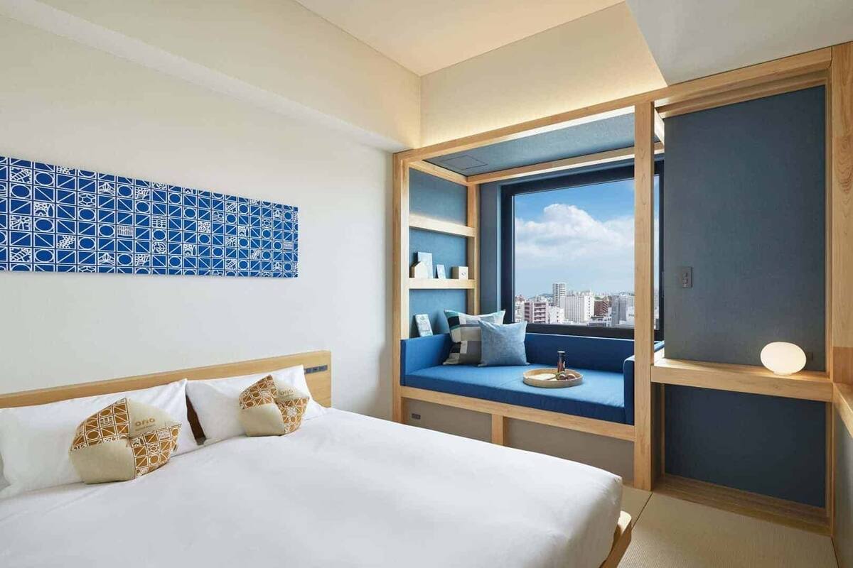 Une chambre d’hôtel avec un lit, un coin salon offrant une vue sur la ville et un mur orné d’un motif bleu.
