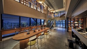 A modern interior with a long dining table, multiple chairs, a staircase, and a bookshelf. - OMO5 Okinawa Naha by Hoshino Resorts (Naha)