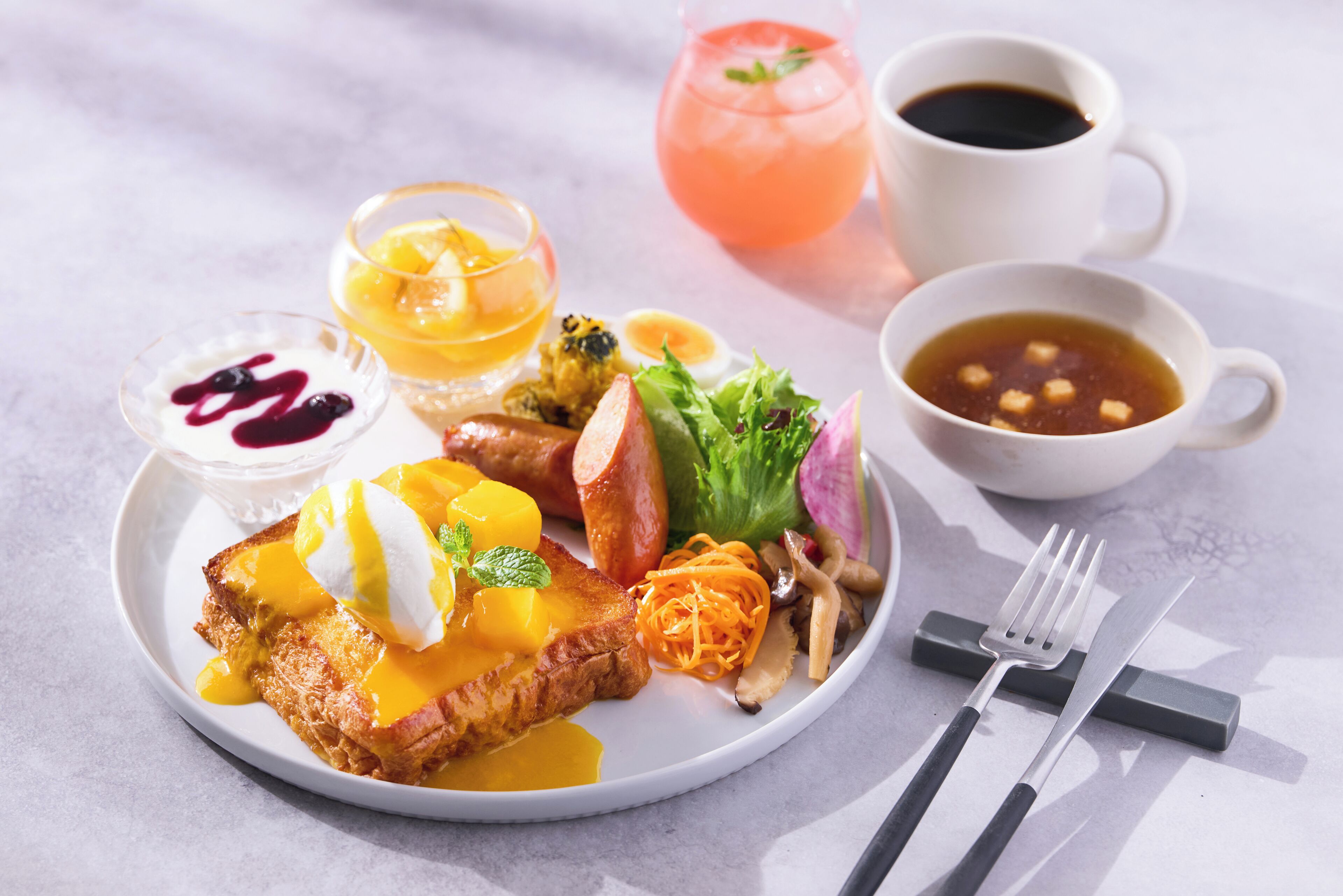 A breakfast plate with toast, eggs, fruit, and vegetables. There are also two cups of coffee and a glass of juice.