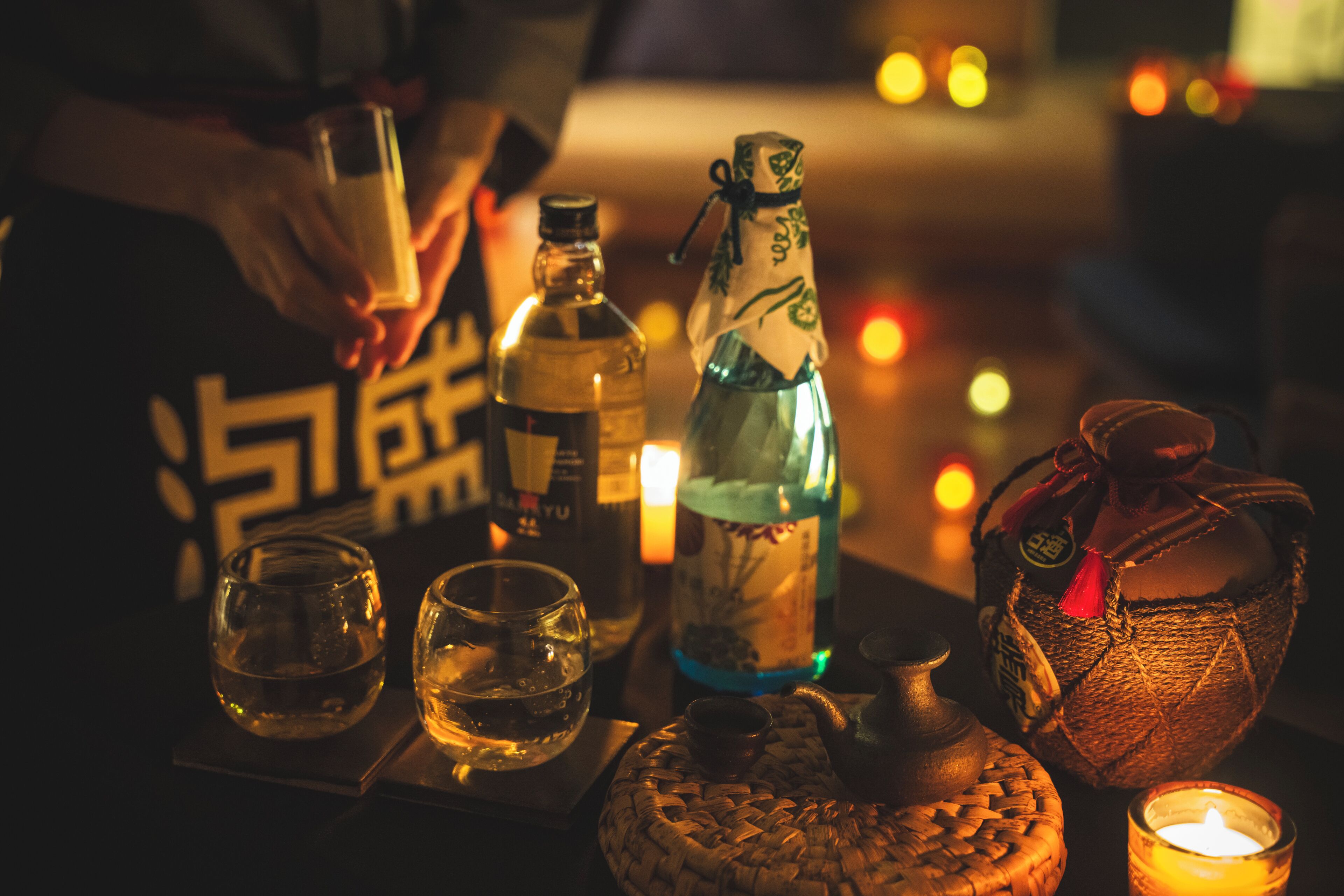 A dimly lit bar setting with a bottle, glasses, and a candle.