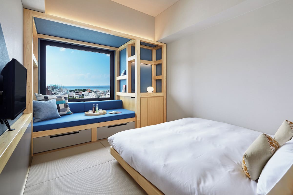 Une chambre moderne dotée d’une grande fenêtre, d’un coin salon intégré et d’un lit.