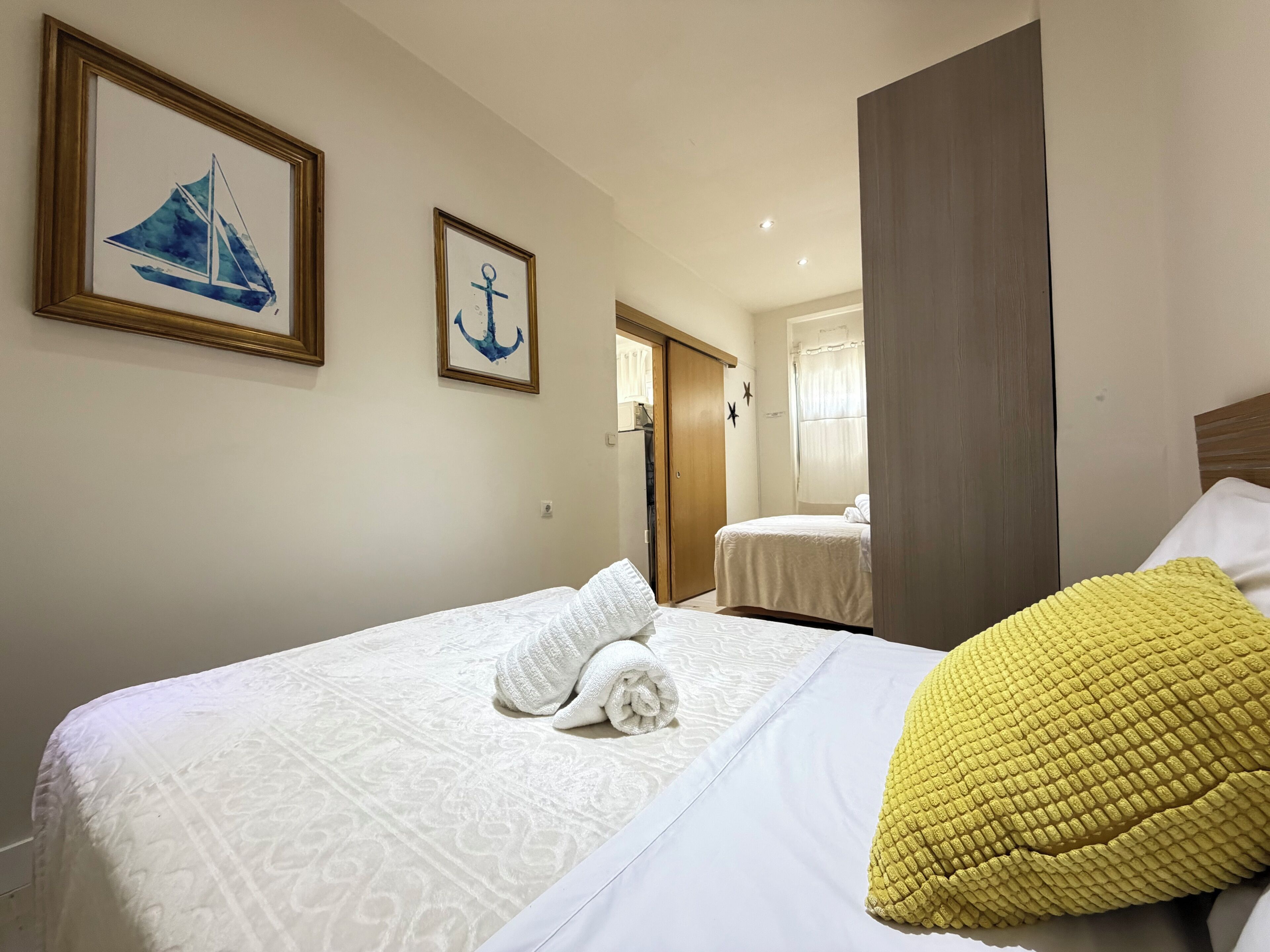 A hotel room with a bed, a yellow pillow, a white towel, and two framed pictures on the wall.