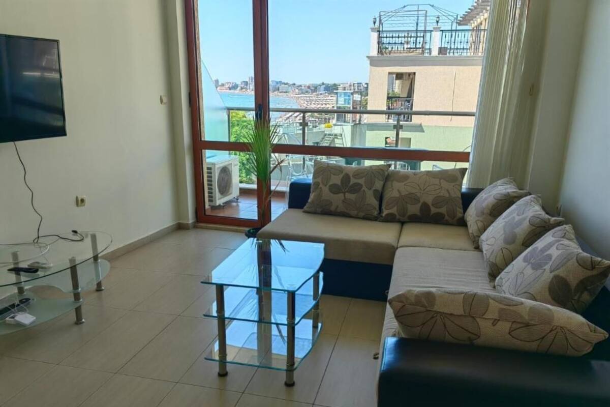 A living room with a sofa, a glass coffee table, and a TV mounted on the wall.