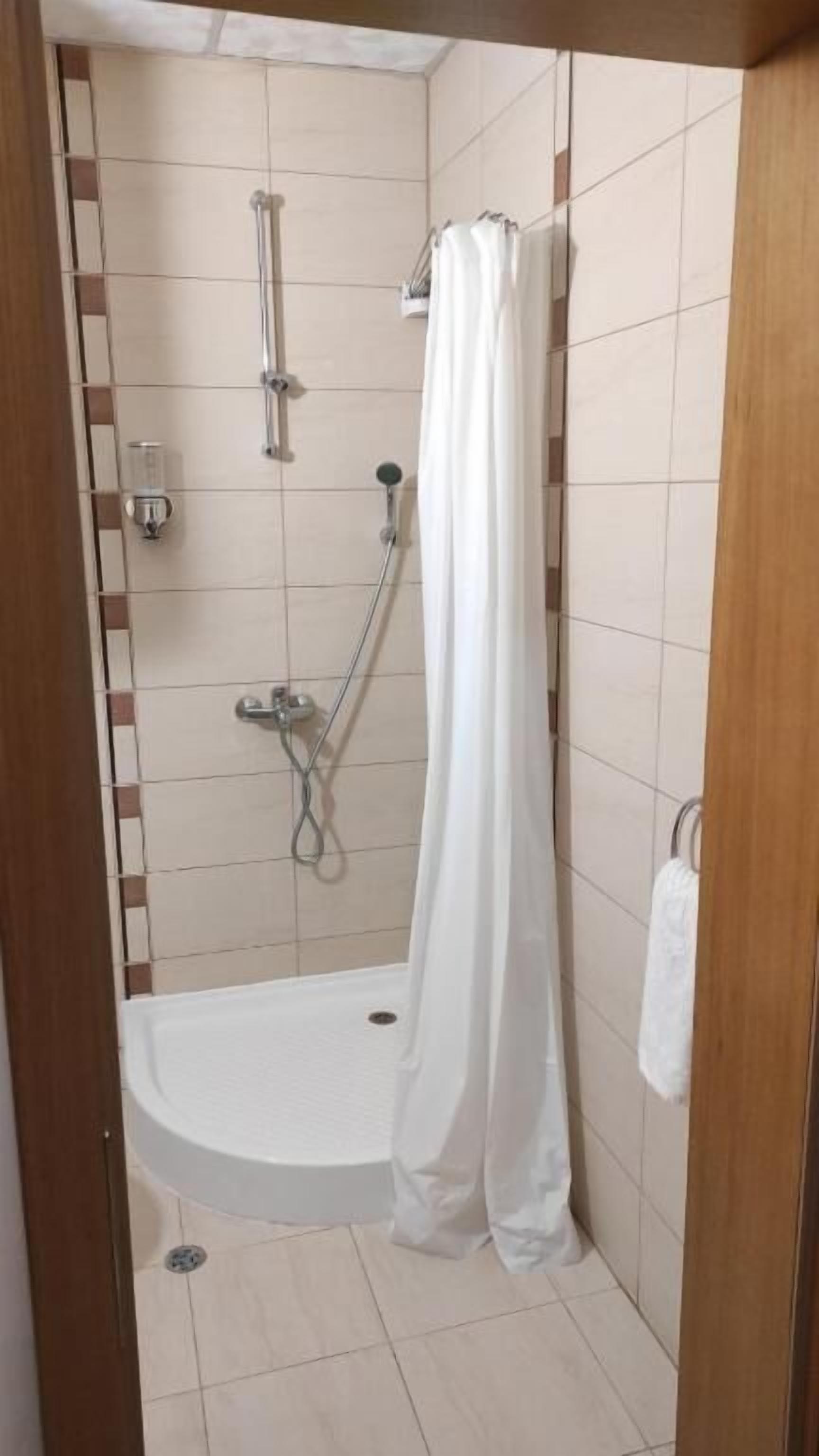 Una ducha con cortina blanca, cabezal de ducha de mano y grifo empotrado.