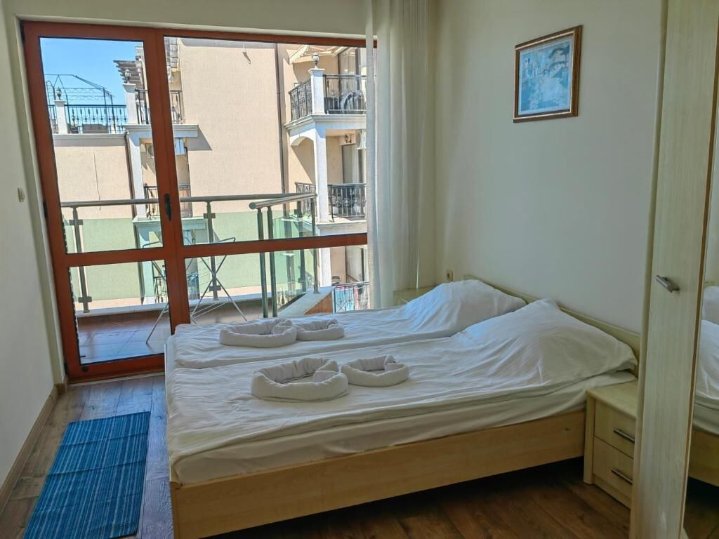 Une chambre à coucher avec un lit, une table de chevet, une fenêtre donnant sur des balcons et un tableau encadré au mur.