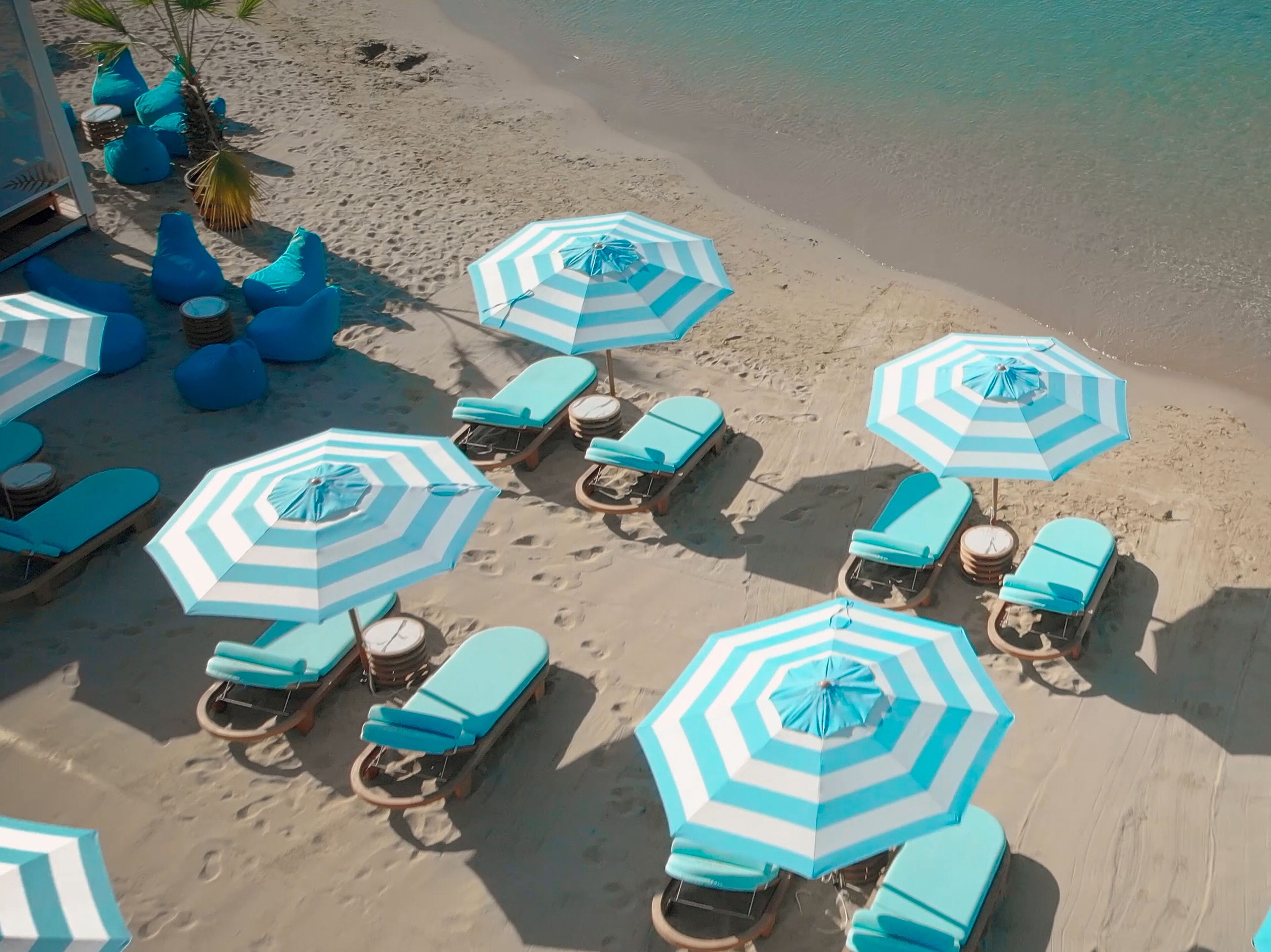 Ein Strand mit mehreren Liegestühlen und gestreiften Sonnenschirmen.
