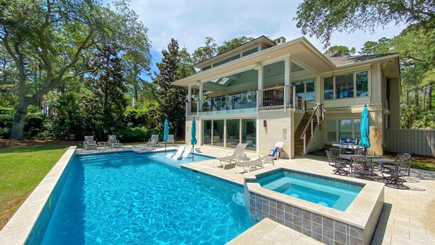 A two-story house with a swimming pool, outdoor furniture, and a patio area.