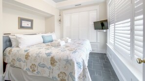 A bedroom with a bed, a mounted TV, and a window with blinds.