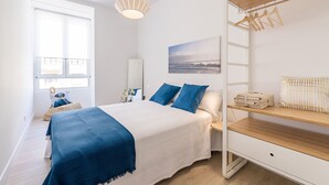 A bedroom with a bed, a bedside table, a hanging rack, and a window. - Free Soul by FeelFreeRentals (San Sebastian)
