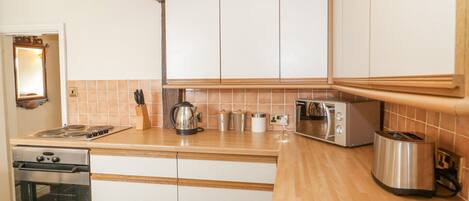 Una cocina con armarios blancos, encimera de madera, estufa, microondas y tostadora.