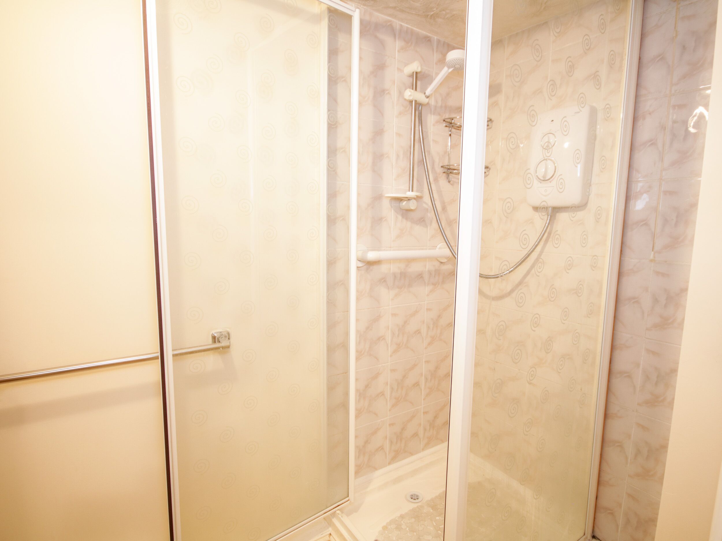 A glass-enclosed shower with a handheld showerhead and a wall-mounted control panel.