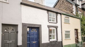 A two-story building with a blue door and a white door, a small window, and a green awning. - Tudor Cottage (Conwy)