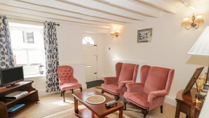 A living room with a television, two pink armchairs, a wooden coffee table, and a patterned rug. - Tudor Cottage (Conwy)