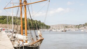 A docked sailing ship with masts and rigging, surrounded by calm water and a marina with other boats. - Tudor Cottage (Conwy)
