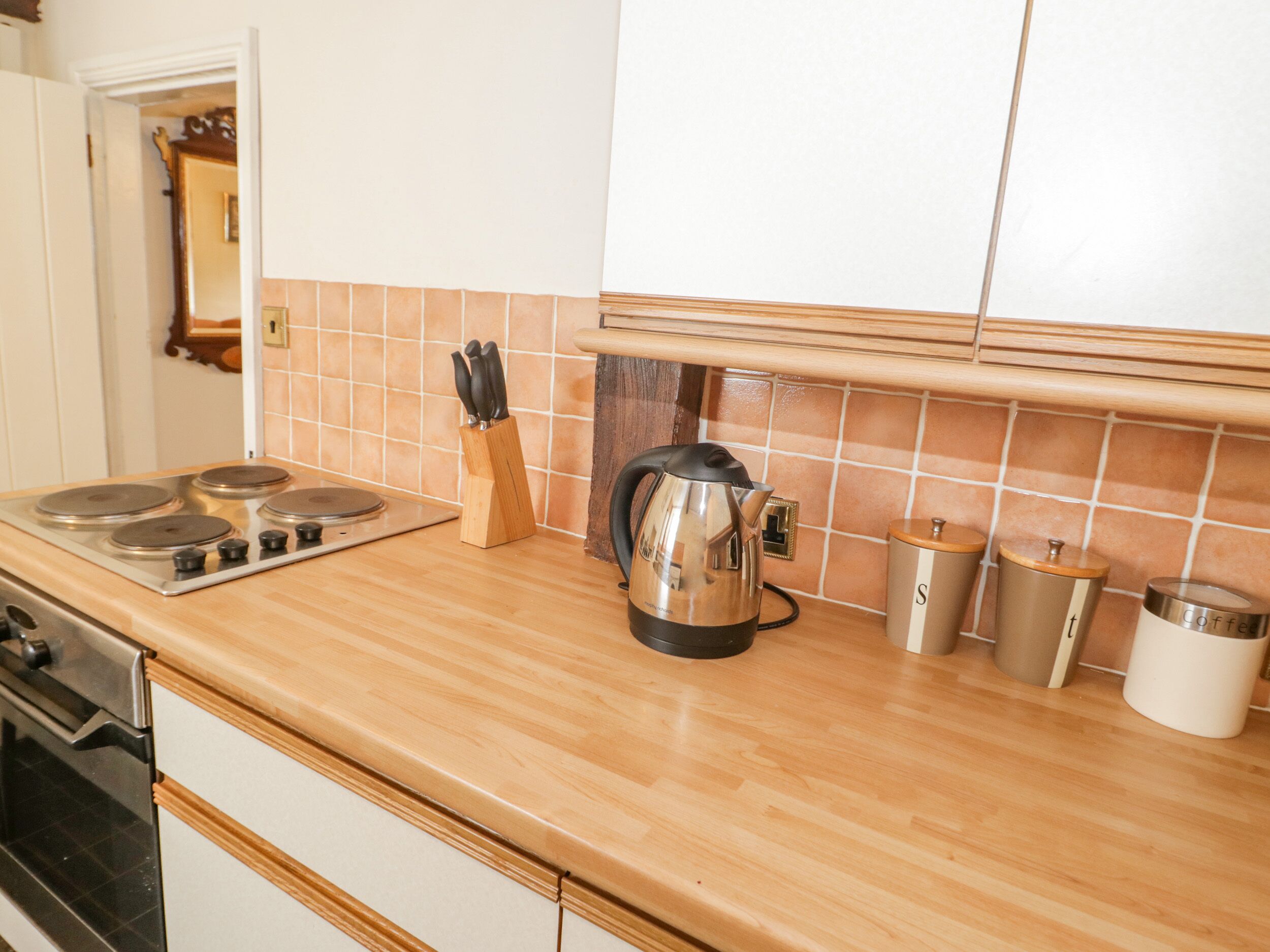 A kitchen with a wooden countertop, a stove, a kettle, and a coffee maker.