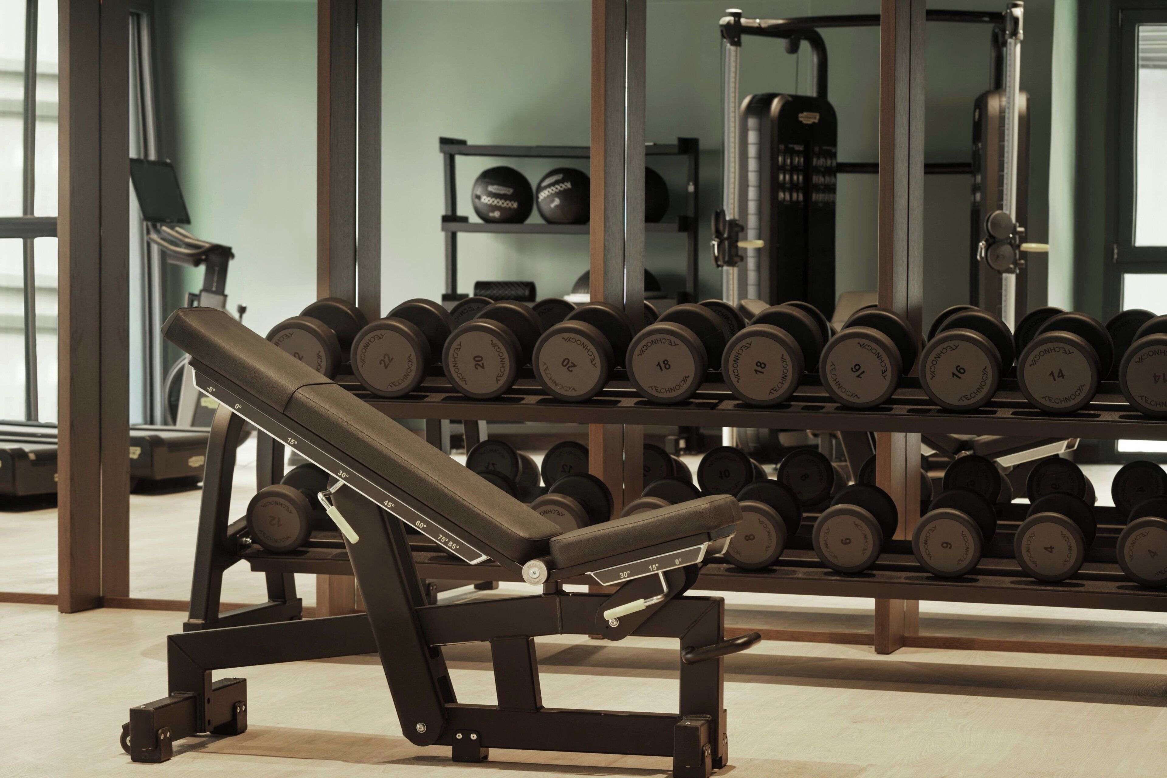 Un gimnasio con una prensa de banca y un estante con mancuernas.
