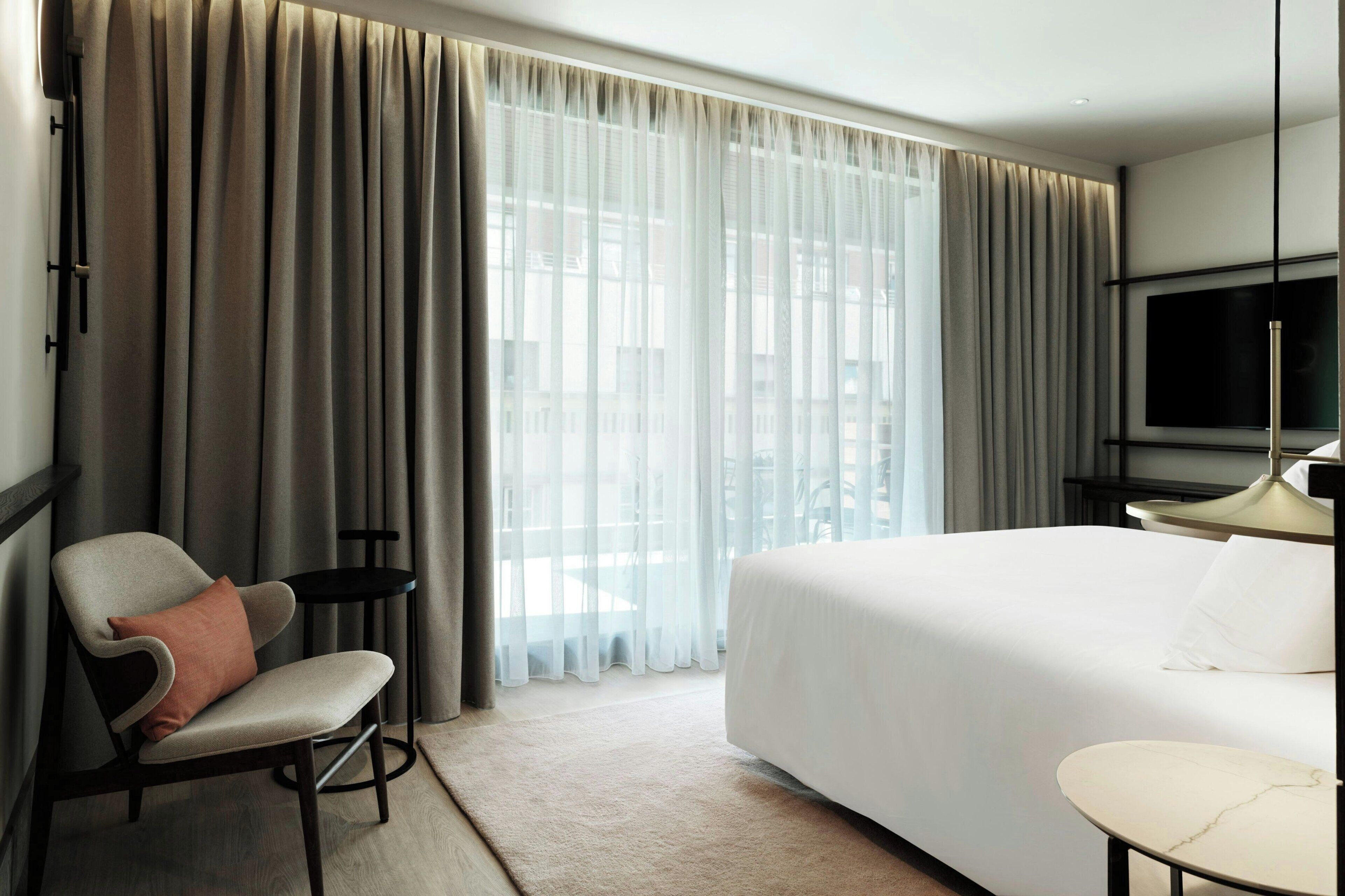 Una habitación de hotel con cama, una silla, una mesita y un televisor.