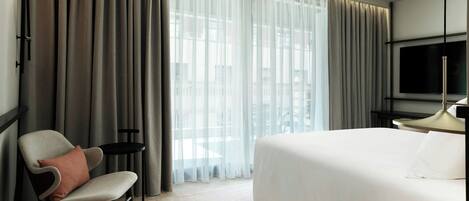 Una habitación de hotel con cama, una silla, una mesita y un televisor.