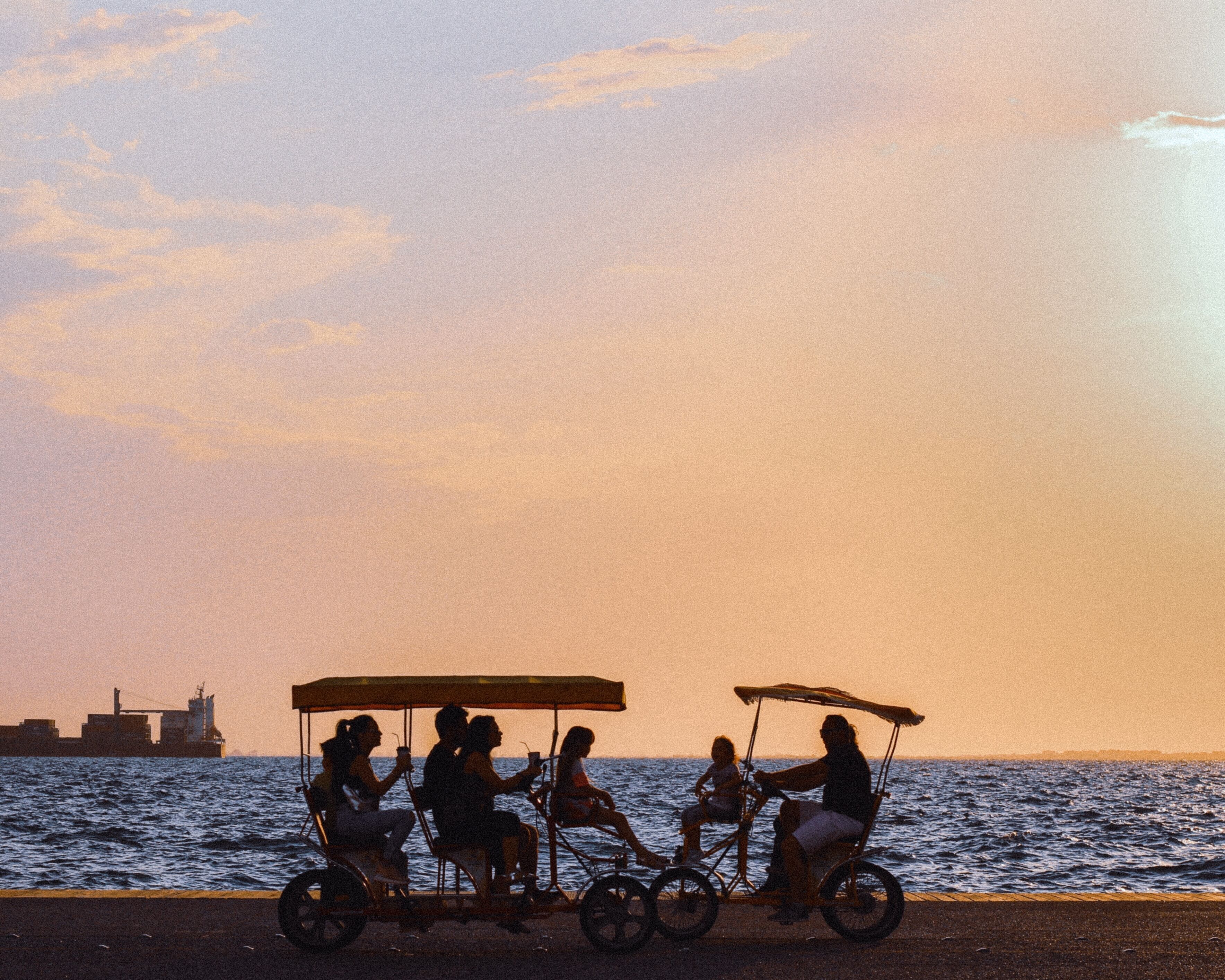 Une scène de coucher de soleil avec un groupe de personnes sur un tricycle, près de l’eau.