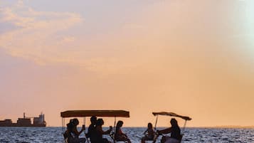 Une scène de coucher de soleil avec un groupe de personnes sur un tricycle, près de l’eau.