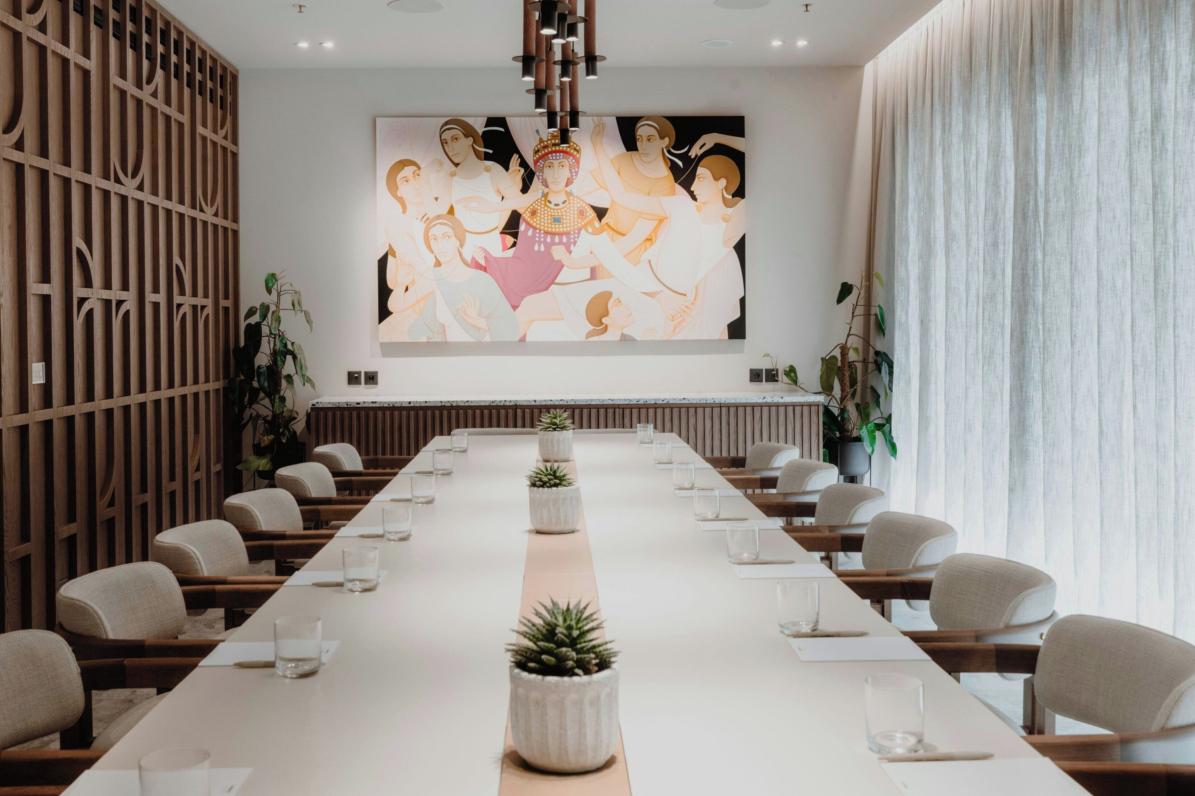 Ein Konferenzraum mit langem Tisch, Stühlen und einem großen Wandgemälde.