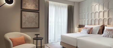 A modern hotel room with a sofa, two beds, a small table, and decorative wall art.
