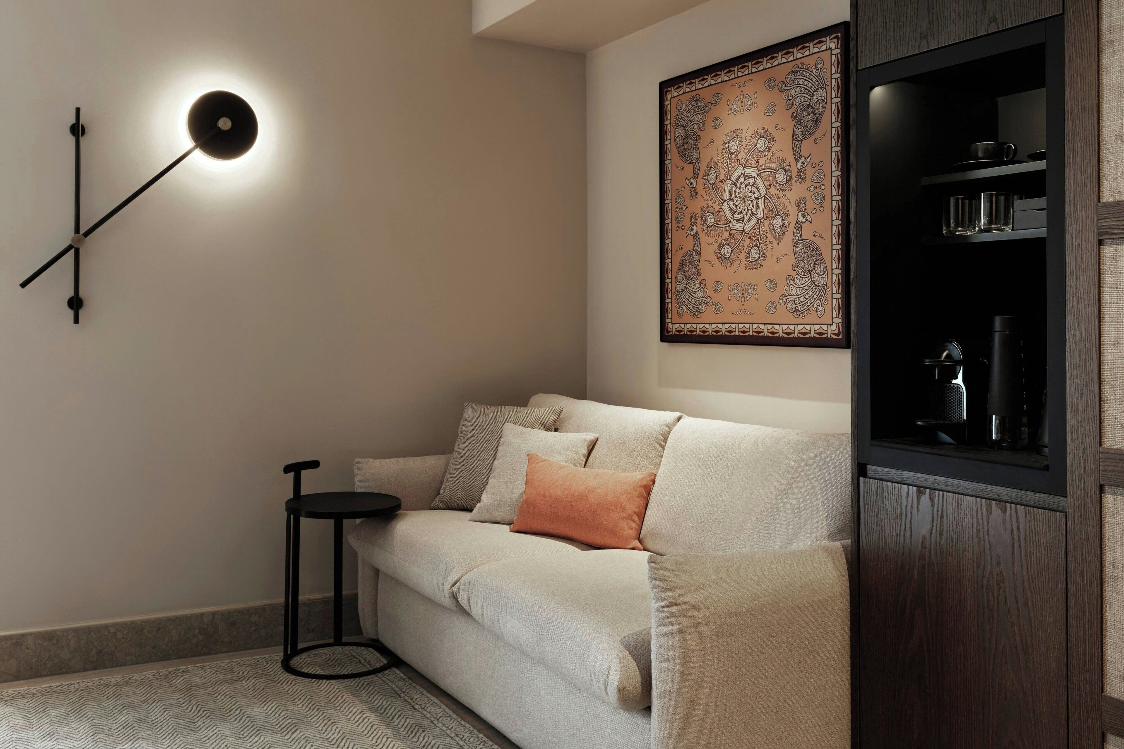 A modern living room with a sofa, a side table, a wall-mounted light, and a decorative wall hanging.
