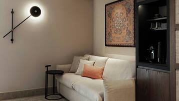 A modern living room with a sofa, a side table, a wall-mounted light, and a decorative wall hanging.