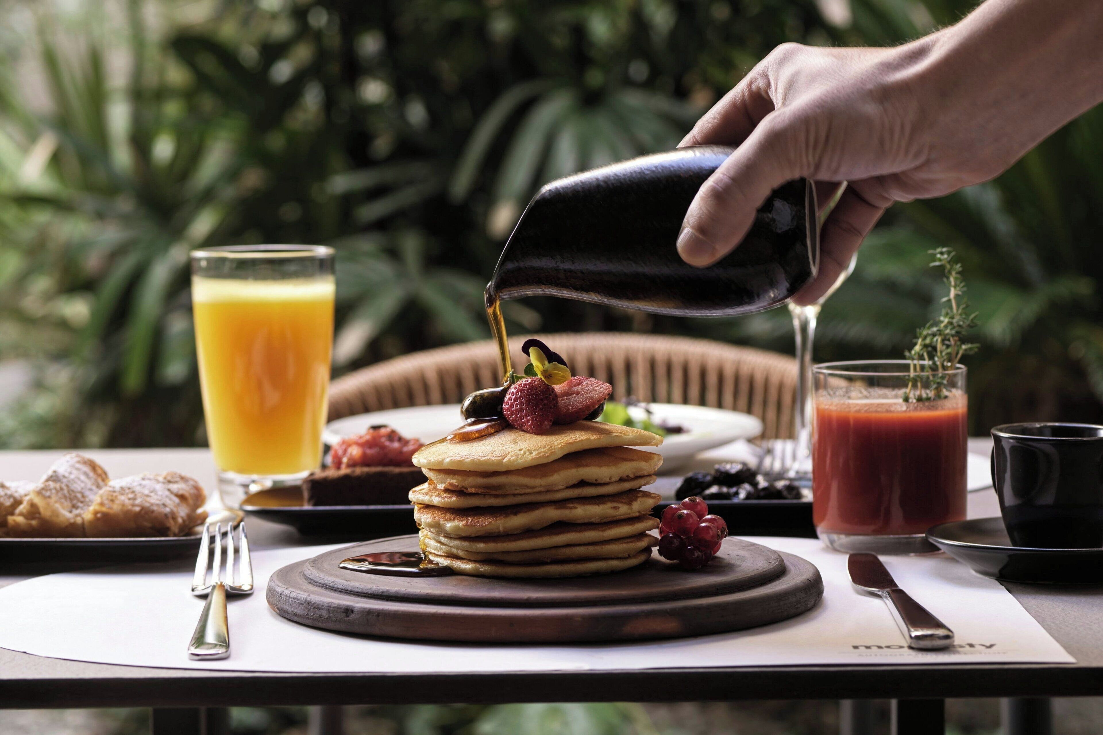 En frukostuppdukning med pannkakor, frukt och drycker på ett bord.