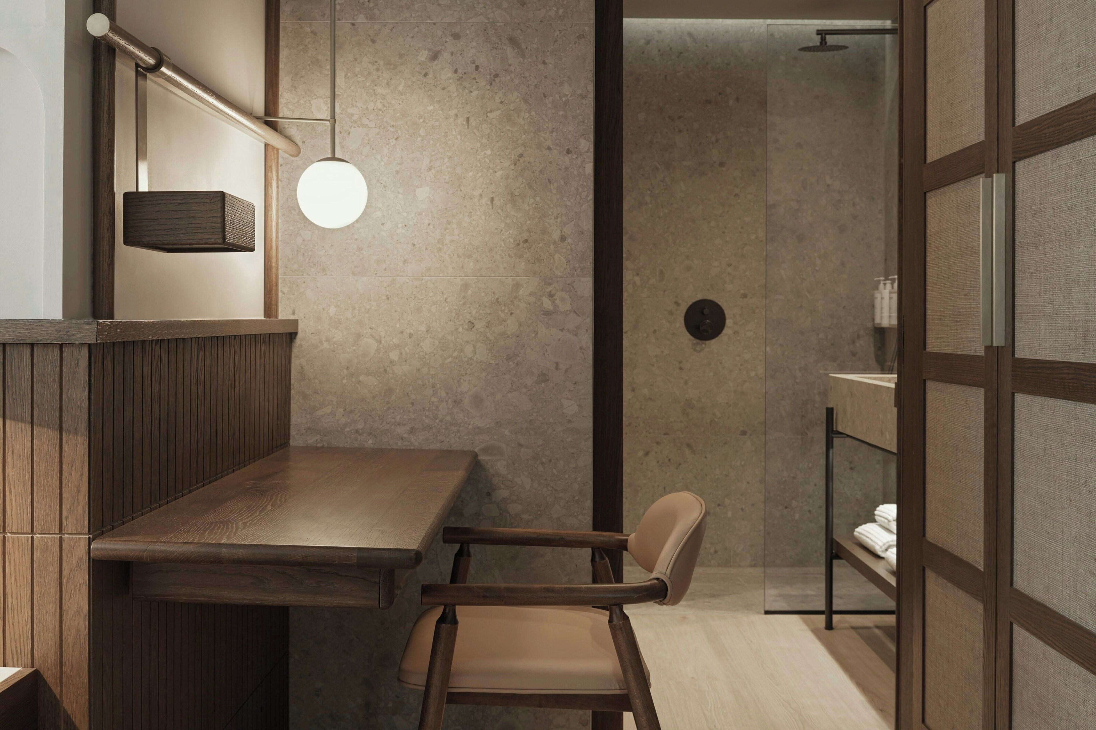A modern bathroom with a wooden vanity, a chair, a towel rack, and a glass shower enclosure.