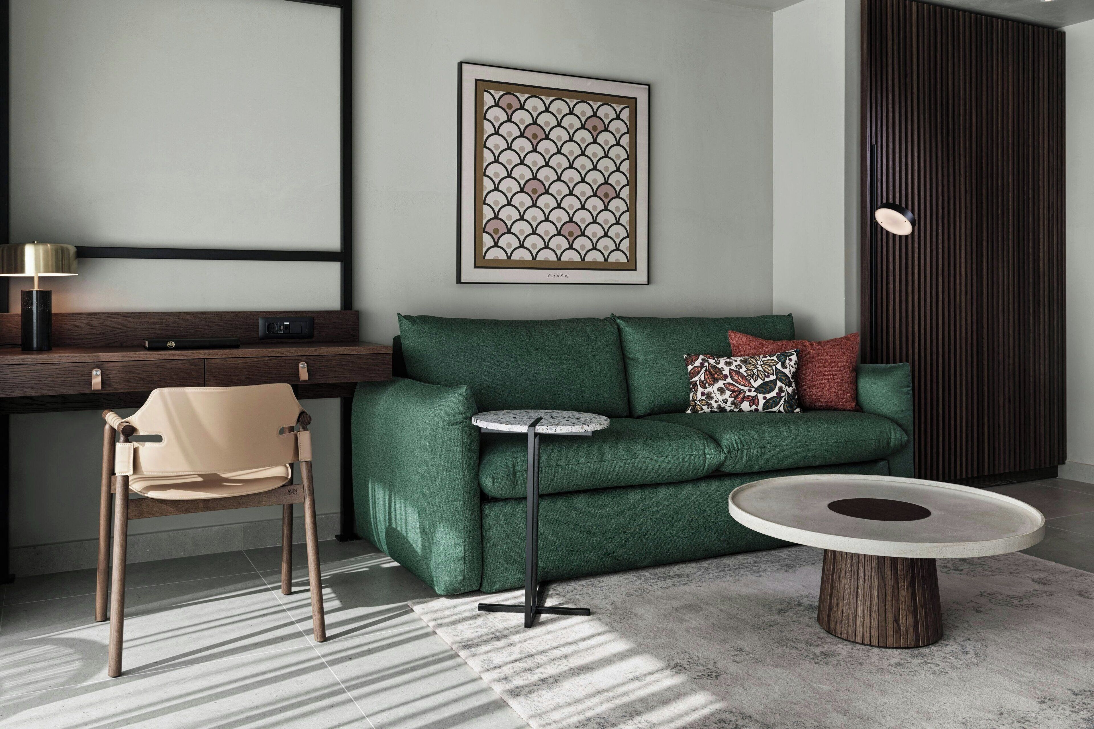 A modern living room with a green sofa, a round coffee table, a beige chair, and a framed artwork on the wall.