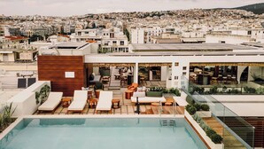 A rooftop pool area with lounge chairs, a wooden deck, and a view of a cityscape. - MonAsty, Thessaloniki, Autograph Collection (Thessaloniki)